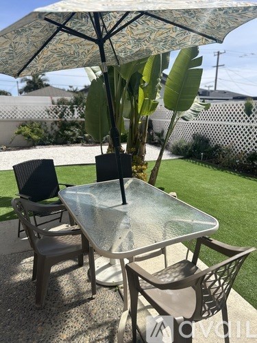 A glass table with chairs and an umbrella is set up on a patio.
