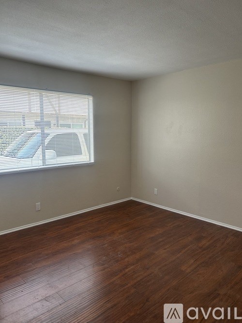 A room with wooden flooring and a window overlooking a parking lot.