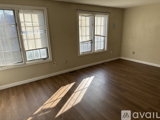 A room with wooden floors and two windows with blinds.