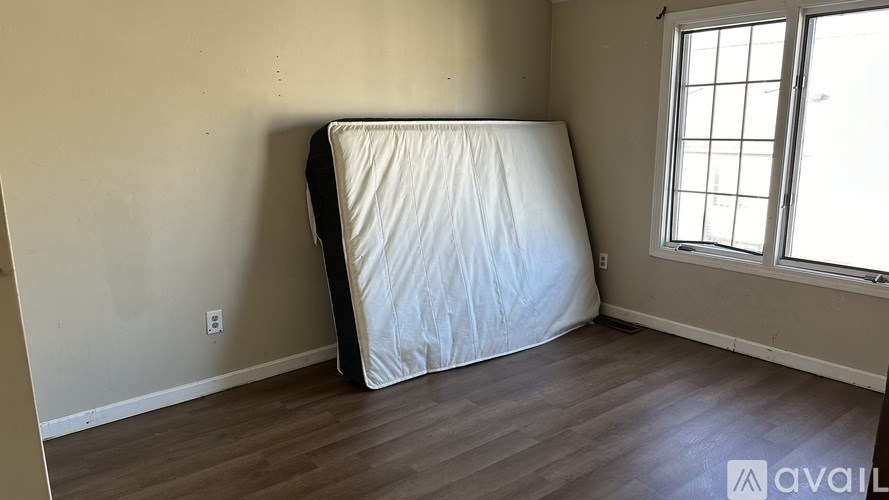 A white mattress is on the floor of a room with a window.
