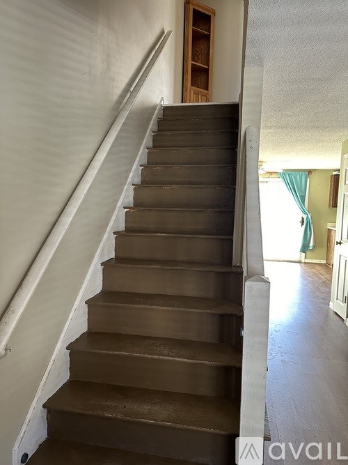A staircase with a wooden handrail and brown steps leading to a doorway.