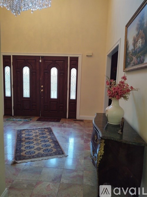 A hallway with a chandelier, a rug, and a vase of flowers.