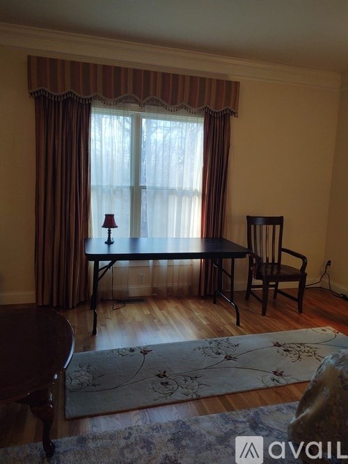 A table with a lamp and a chair in front of a window with curtains.