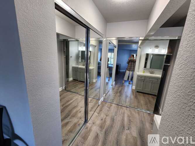 A person is standing in a room with a mirrored wall and wooden flooring.