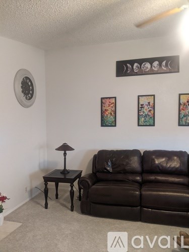 A living room with a brown leather couch, a small table with a lamp, and three framed pictures on the wall.
