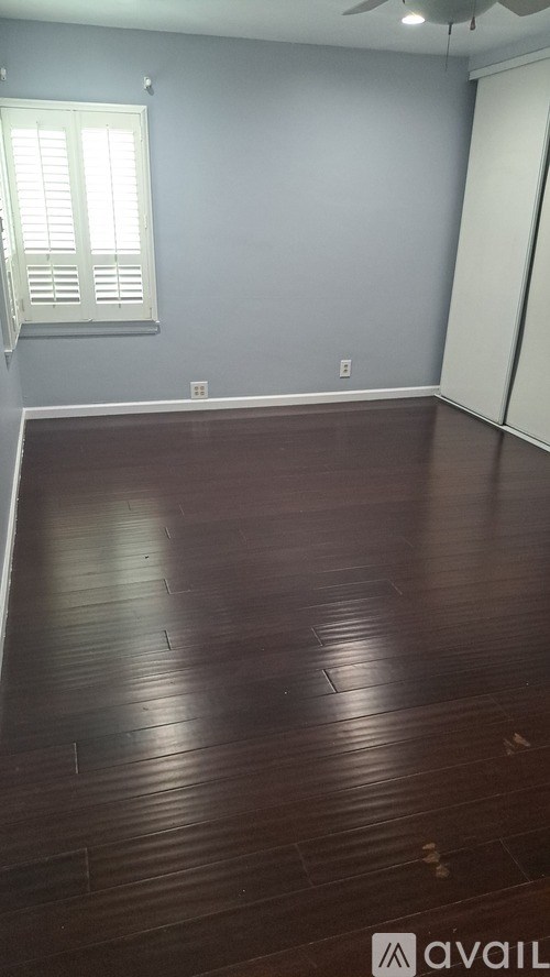 A room with wooden flooring and a window with white blinds.