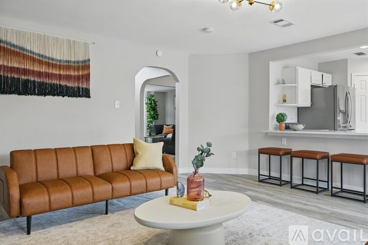 A living room with a brown leather sofa, a white coffee table, and a wall hanging.