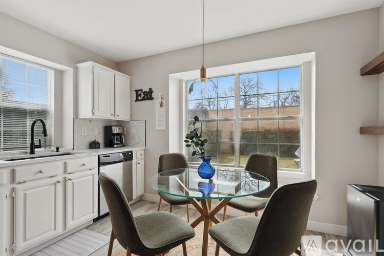 A kitchen with a glass table and chairs, a window with a view of a field, and a sign that says "Eat".