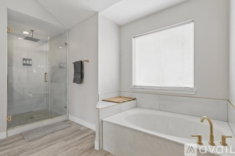 A modern bathroom with a glass shower stall and a bathtub with a gold faucet.