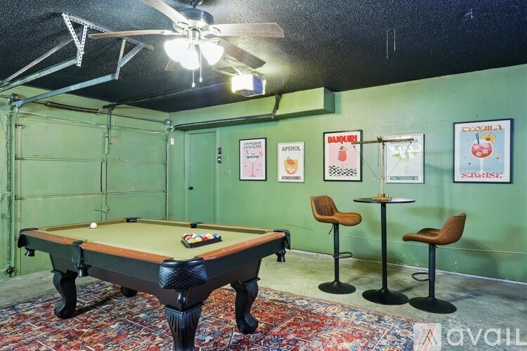 A pool table is in the middle of a room with a green wall and a fan.