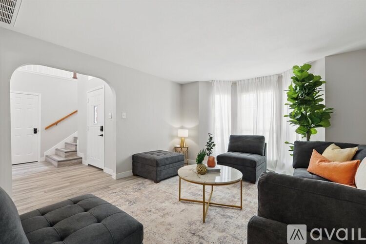 A living room with a grey couch, a black ottoman, a coffee table, and a plant.