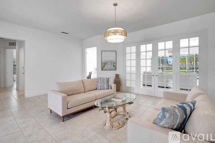 A living room with a beige couch, a glass coffee table, and a chandelier.