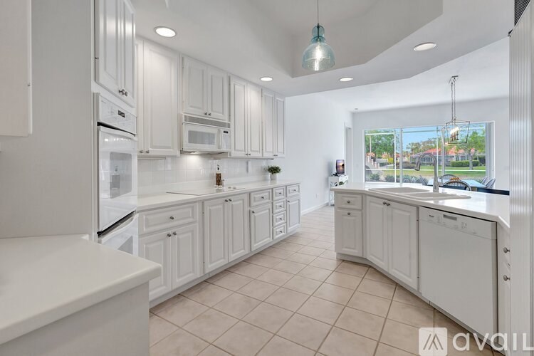 A kitchen with white cabinets and appliances, a large island, and a view of the outdoors through a window.
