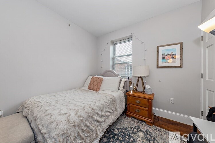 A bedroom with a bed, nightstand, and a window.