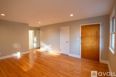 A room with wooden floors and white walls has a door on the right and two doors in the background.