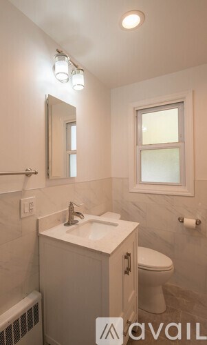 A bathroom with a toilet, sink, mirror, and window.