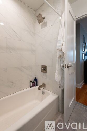 A white bathroom with a tub and a towel hanging on the door.