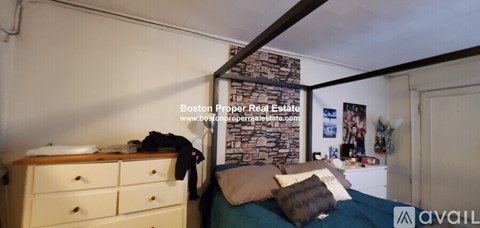 A bedroom with a bed, dresser and a stone wall.