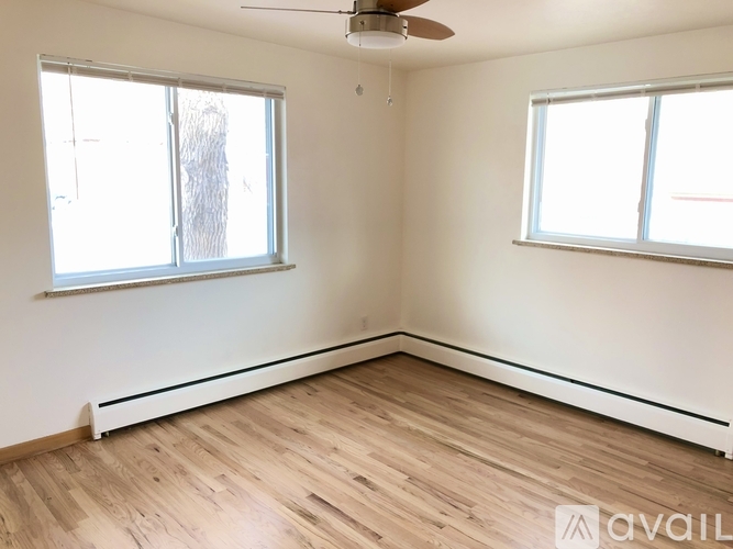 A room with wooden flooring and two windows.