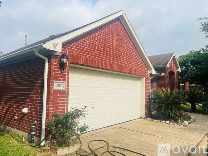 A red brick house with a white garage door and a black lamp on the wall.