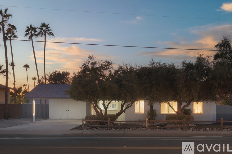 A house with a white exterior and a brown roof is surrounded by trees and palm trees.