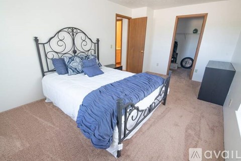 A bed with a black metal headboard and a blue blanket is in a room with a carpeted floor.