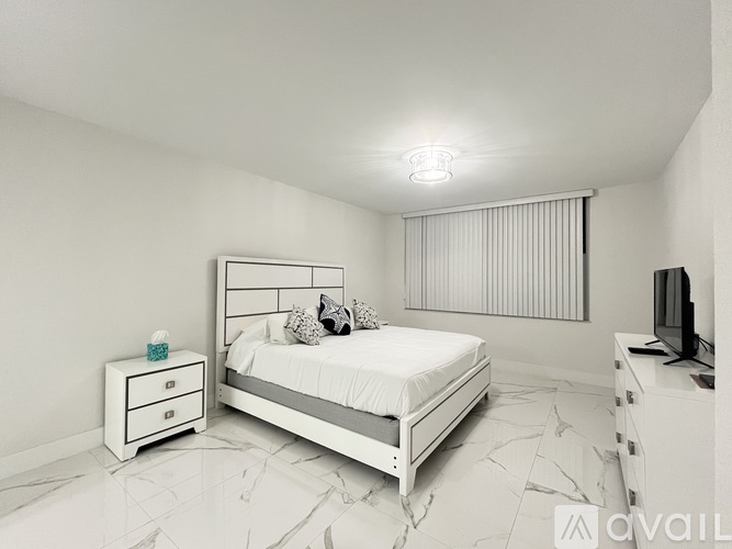 A white bedroom with a bed, nightstand, and television.