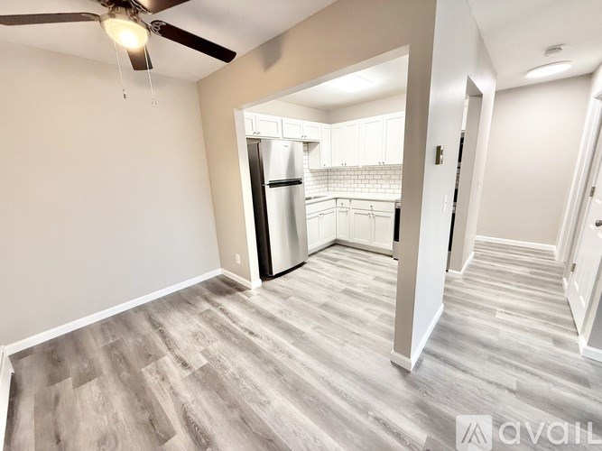 A spacious room with a ceiling fan and a kitchen visible through the open door.