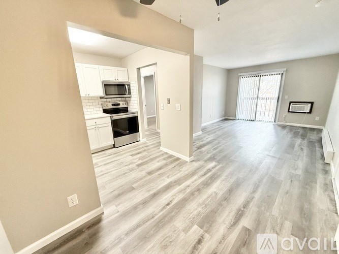A spacious living room with wood flooring and a kitchen area in the background.