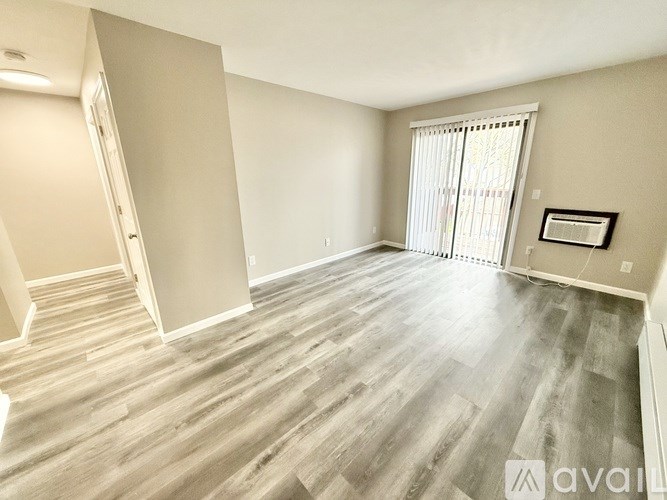 A spacious room with wooden flooring and a window with blinds.