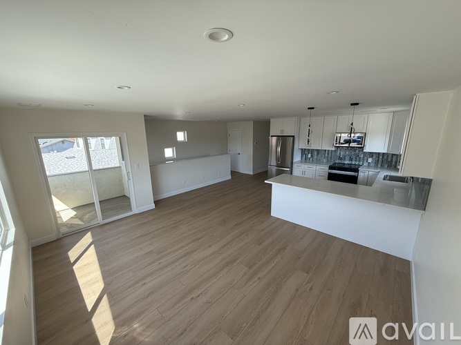 A spacious kitchen with wooden flooring and white walls.