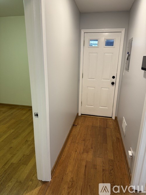 A white door with a black handle is in a hallway with wood floors.