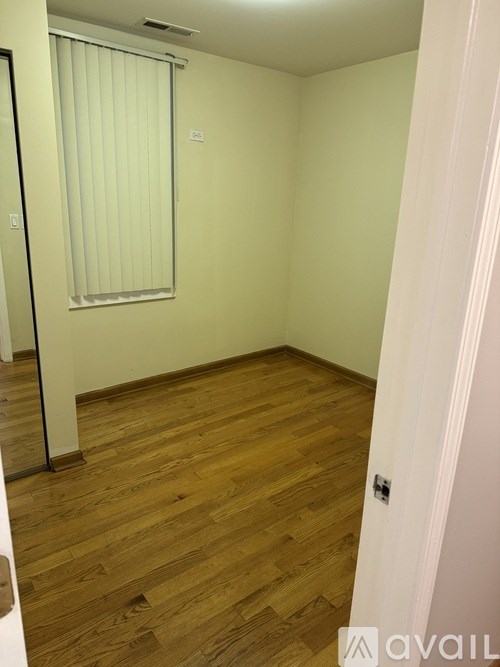 A room with wooden flooring and a window with blinds.