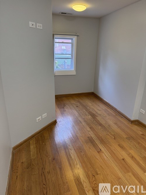 A room with wooden flooring and a window showing a view of a building outside.