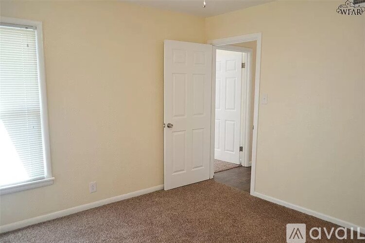 A room with a carpeted floor, a white door, and a window with blinds.