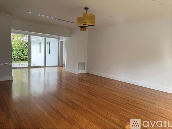 A room with wooden flooring and white walls, with a large window and sliding glass doors.