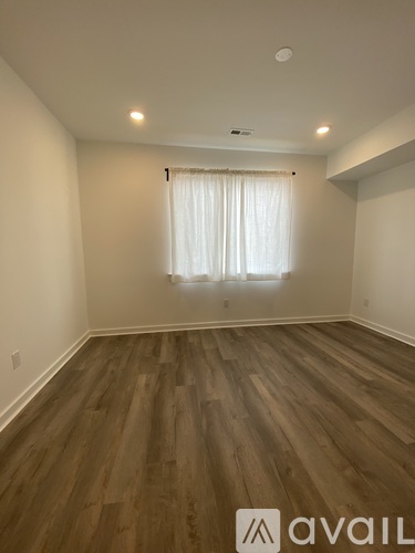 A room with wooden flooring and a window with white curtains.