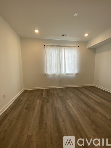 A room with wooden flooring and a window with white curtains.