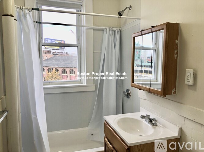 A bathroom with a sink, mirror, and a window showing a view of a building.
