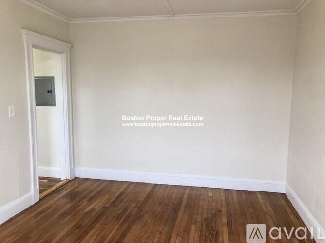 A room with wooden floors and white walls, with a door on the left.