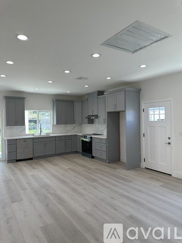 A spacious kitchen with grey cabinets and a white door.