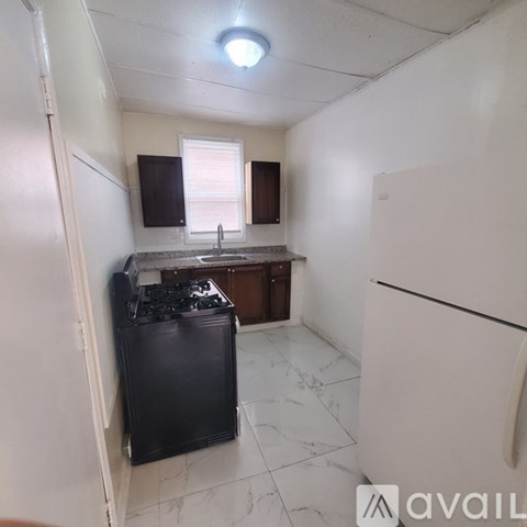 A kitchen with a black fridge, white walls, and a window with blinds.