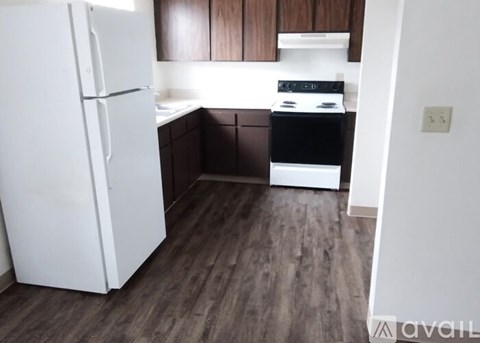 A white refrigerator stands in a kitchen with wooden floors and brown cabinets.
