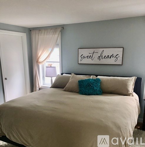 A bedroom with a bed, pillows, and a wall hanging that says "sweet dreams".