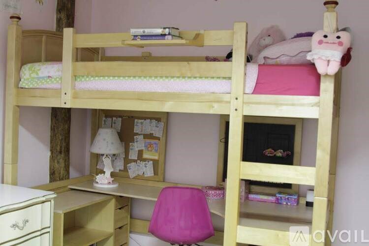 A wooden bunk bed with a pink chair and a white desk with drawers.