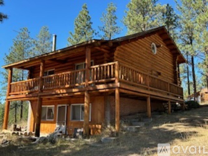 A wooden cabin with a balcony is surrounded by trees.