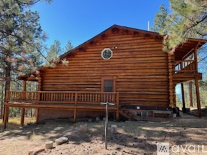 A wooden cabin with a porch and a balcony is surrounded by trees.