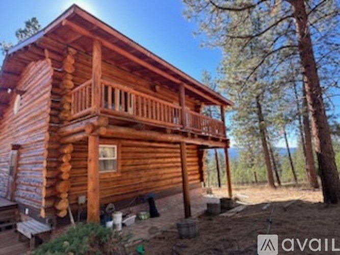 A wooden cabin with a balcony and a porch surrounded by trees.