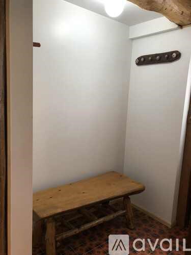A wooden bench sits in a corner of a room with white walls.