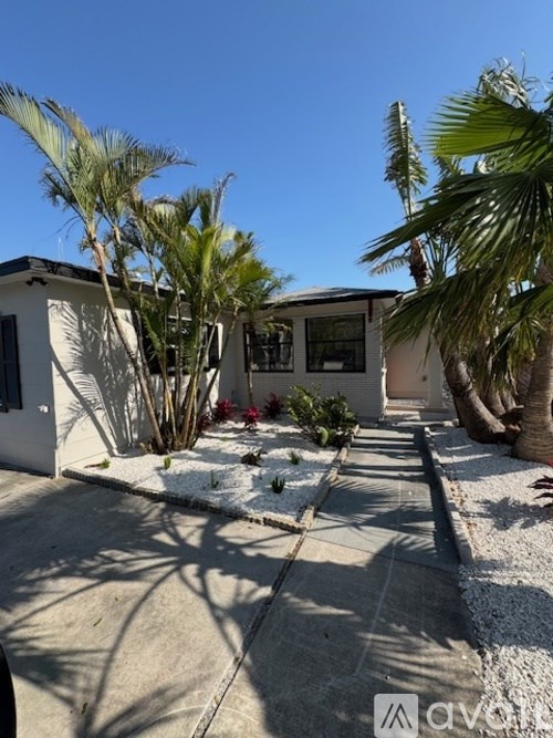 A white house with a black roof is surrounded by palm trees.